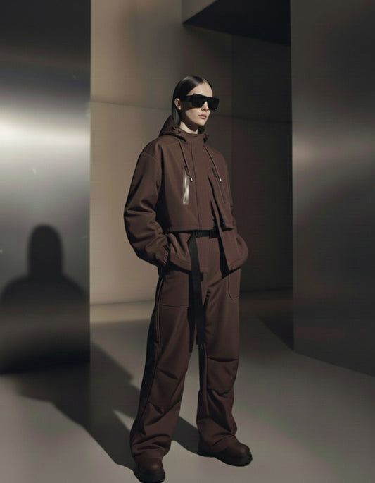 A woman wearing a brown outfit and sunglasses in a minimalistic setting