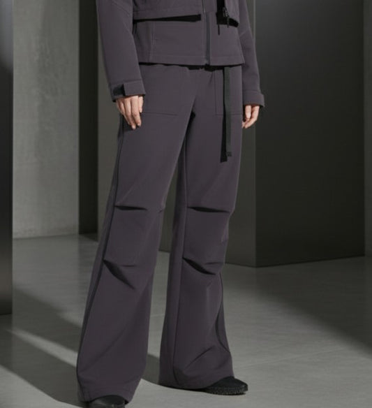 Person wearing a dark gray outfit with wide-leg pants and a jacket in a minimalistic setting.