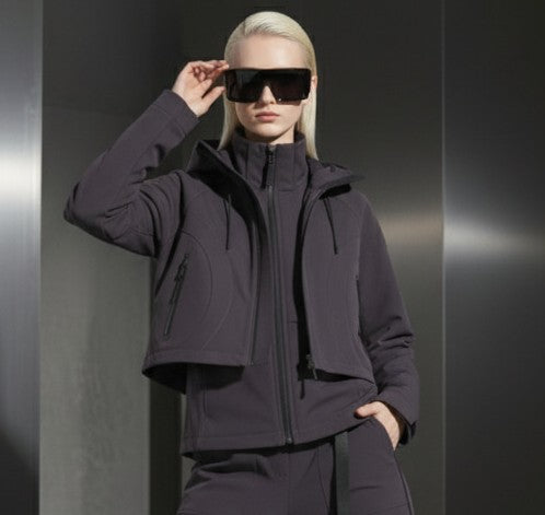 A woman wearing a dark grey jacket and sunglasses against a gray steal background