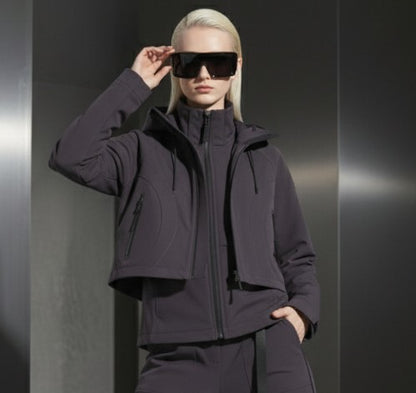 A woman wearing a dark grey jacket and sunglasses against a gray steal background