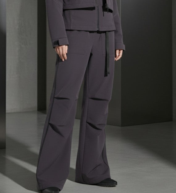 Person wearing a dark gray outfit with wide-leg pants and a jacket in a minimalistic setting.