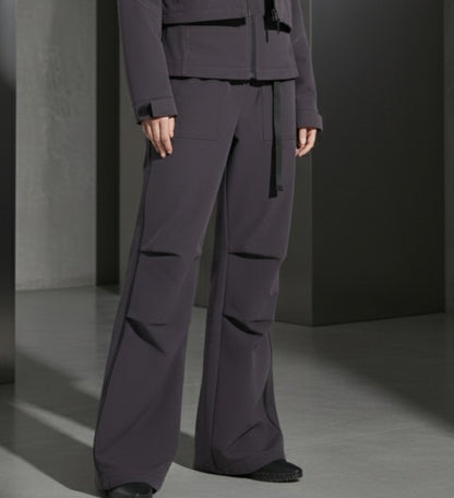 Person wearing a dark gray outfit with wide-leg pants and a jacket in a minimalistic setting.