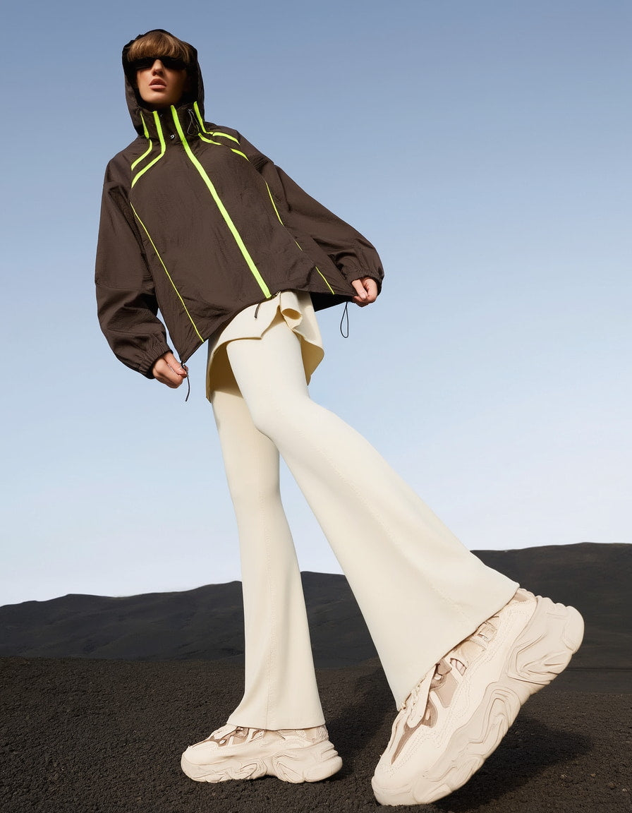 Women wearing a gym jackets for women's with neon green accents, beige pants, and beige sneakers against a clear blue sky.