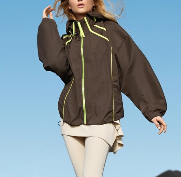 woman wearing a brown activewear jacket with green accents against a clear blue sky