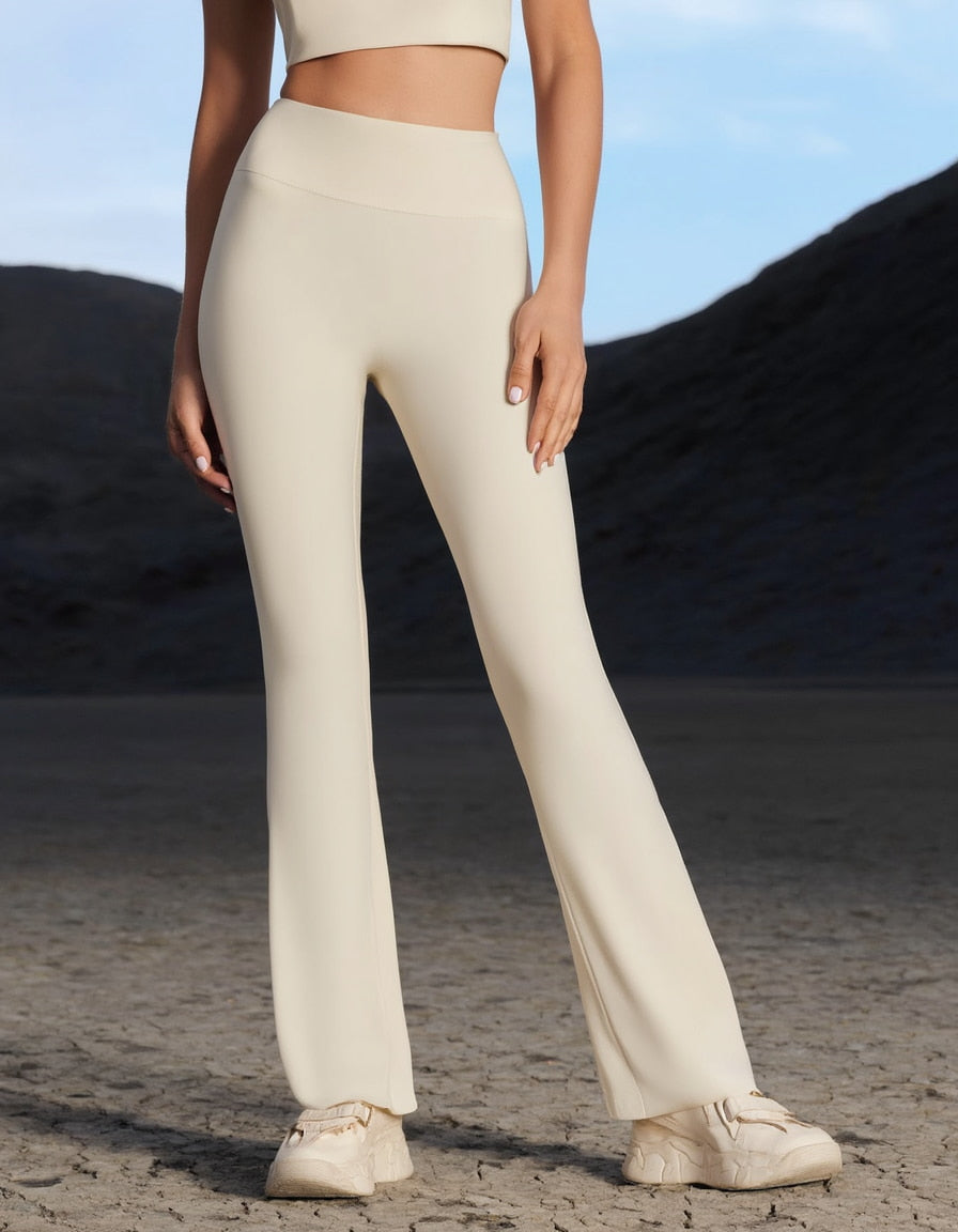 Model wearing beige hot yoga trousers and top, standing on a sandy surface with a blurred natural background