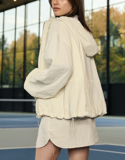Woman wearing a light-colored outfit with a jacket and skirt on an outdoor court.