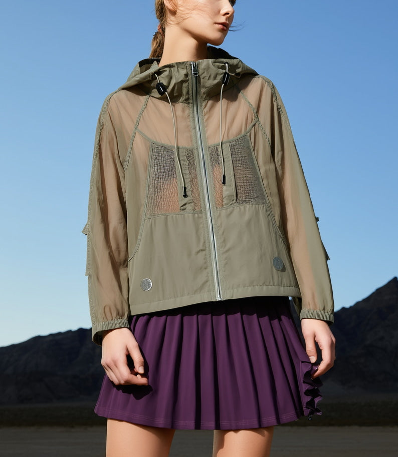 Woman wearing a green sportswear jacket womens with sheer panels over a purple skirt against a blue sky.