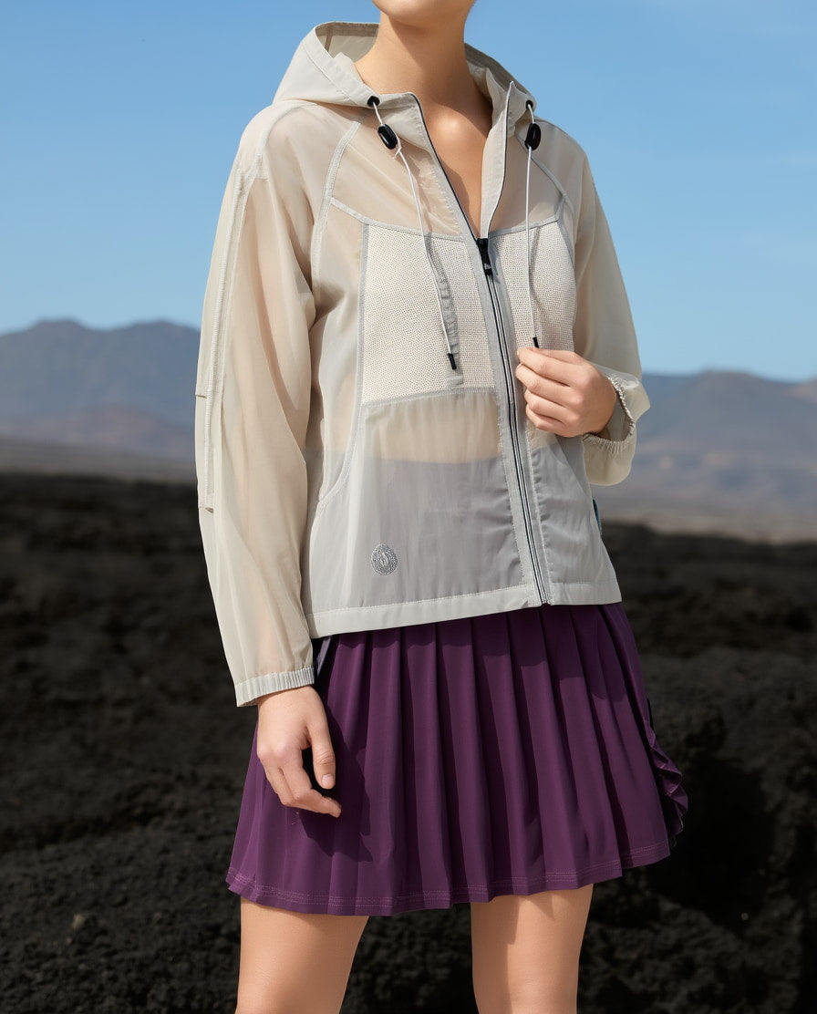 Person wearing a beige light activewear jacket over a purple tennis dress with a mountainous background