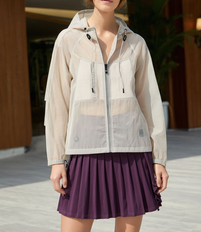 A woman wearing a transparent activewear jacket over a purple tennis skirt outdoors.